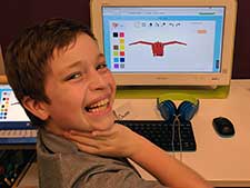 Boy smiling in front of an image of a digital dragon he drew at coding camps