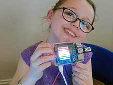 Girl holds raspberry pi with rainbow LEDs she programmed at coding camp