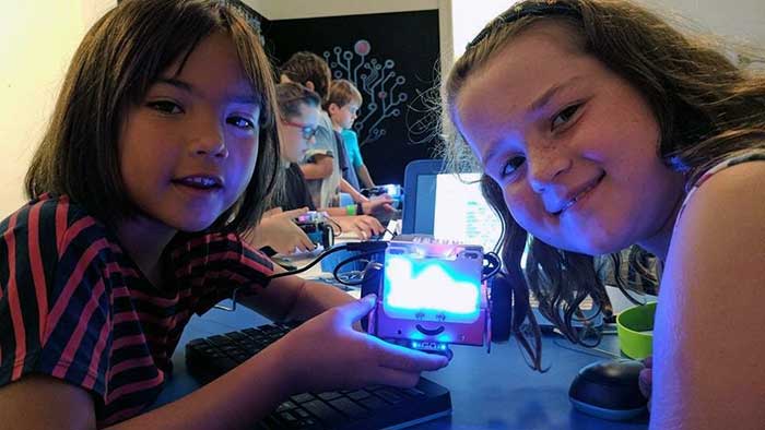 Two girls show off the LED pattern they coded on a robot during our kids coding classes