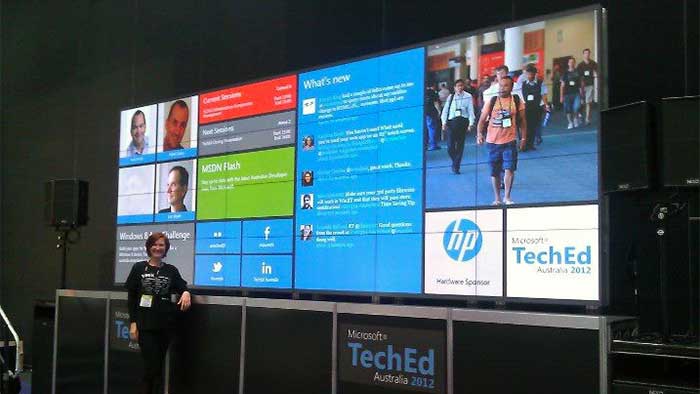 Our coding classes for kids teacher stands in front of a multiscreen interactive display she made for Microsoft